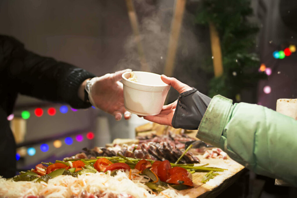 Hand überreicht Becher bei Weihnachtsfeier mit obdachlosen Menschen